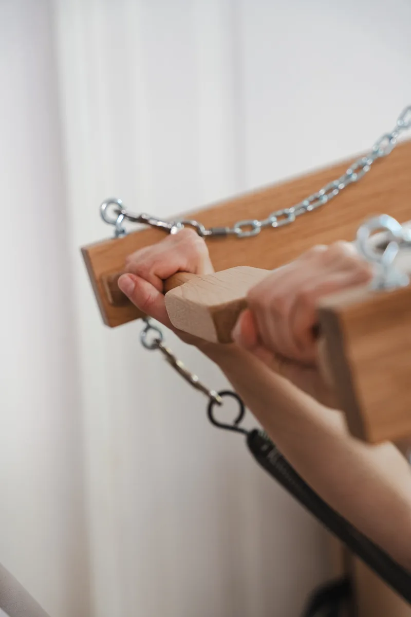 Dłonie trzymające drewniany uchwyt sprzętu pilatesowego